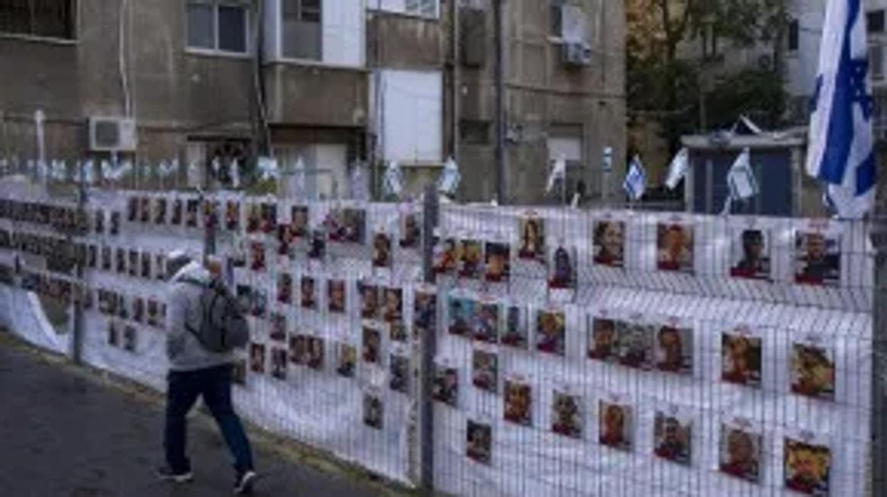 A man passes by a fence with photograph of hostages who were abducted during the October 7 massacre